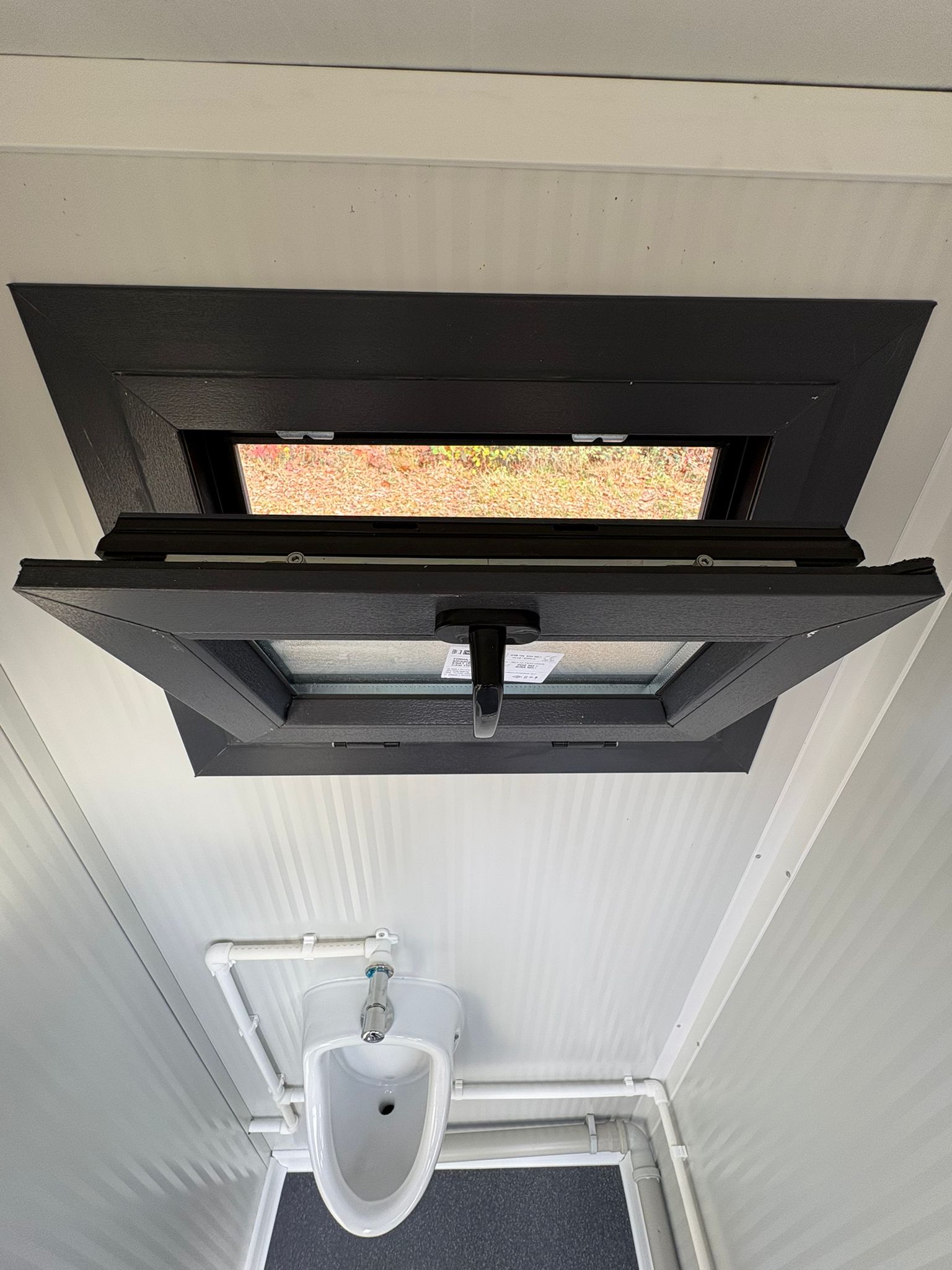 Openstaand draaikiepraam in de urinoirruimte van een toilet- en urinoirunit.