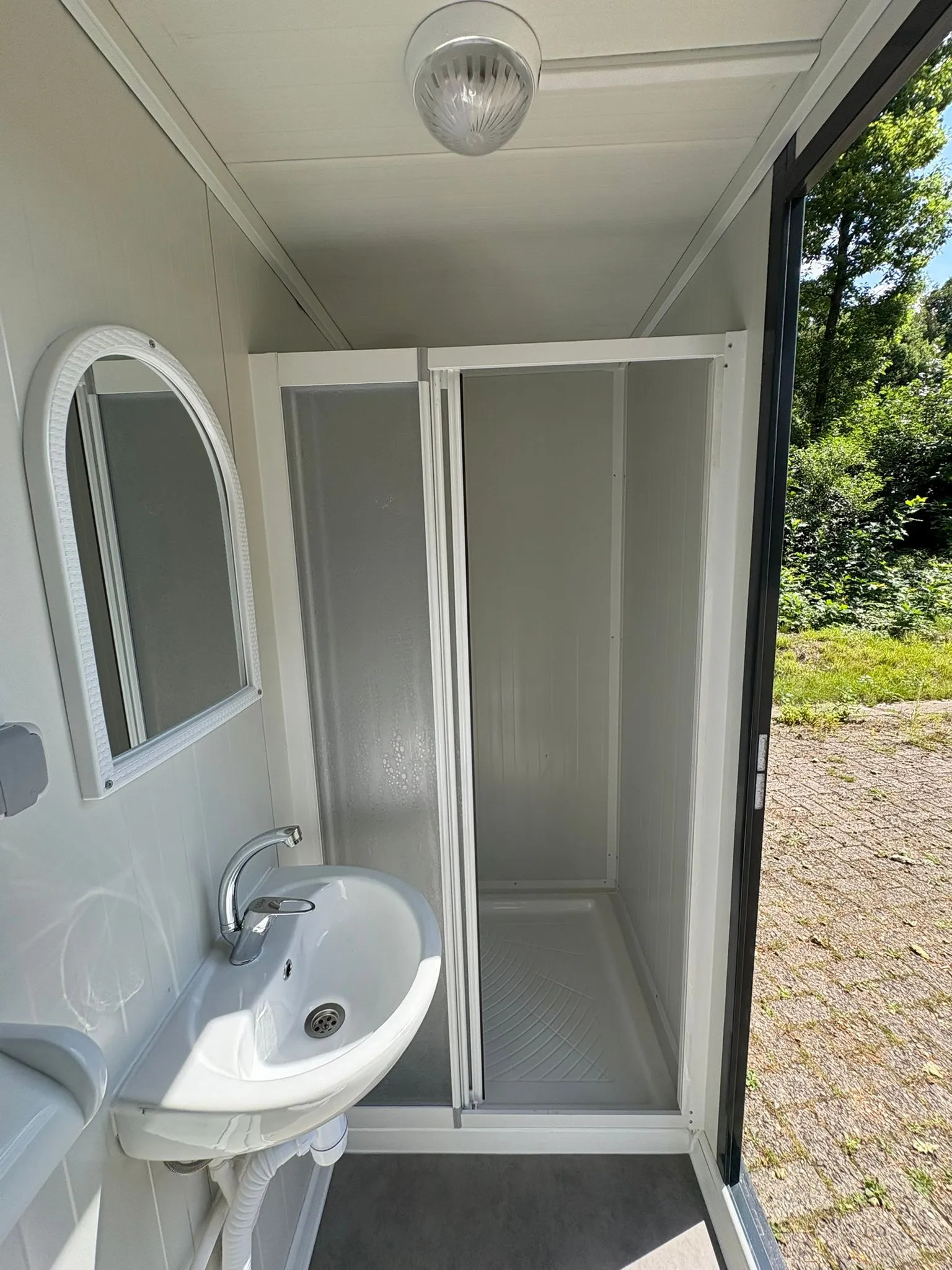 Interior of a portable bathroom unit showing the shower, sink, and mirror.