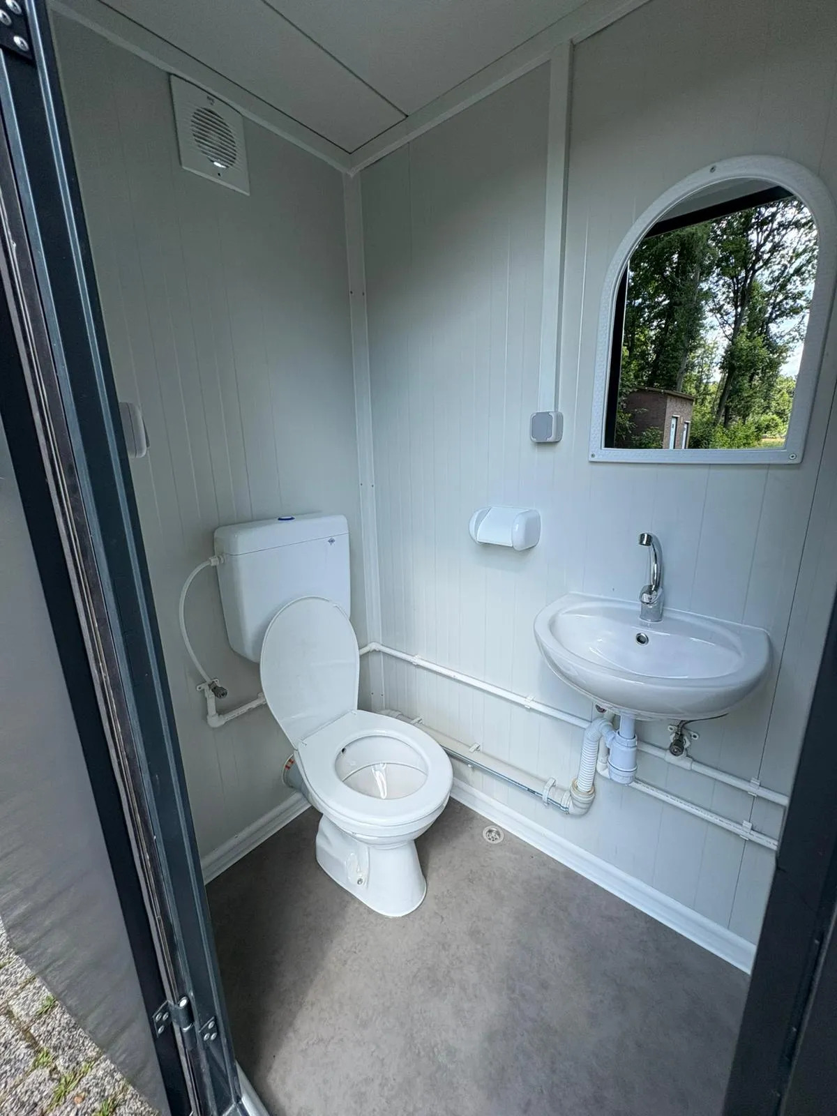 Interior of a portable bathroom unit featuring the toilet, sink, and mirror.
