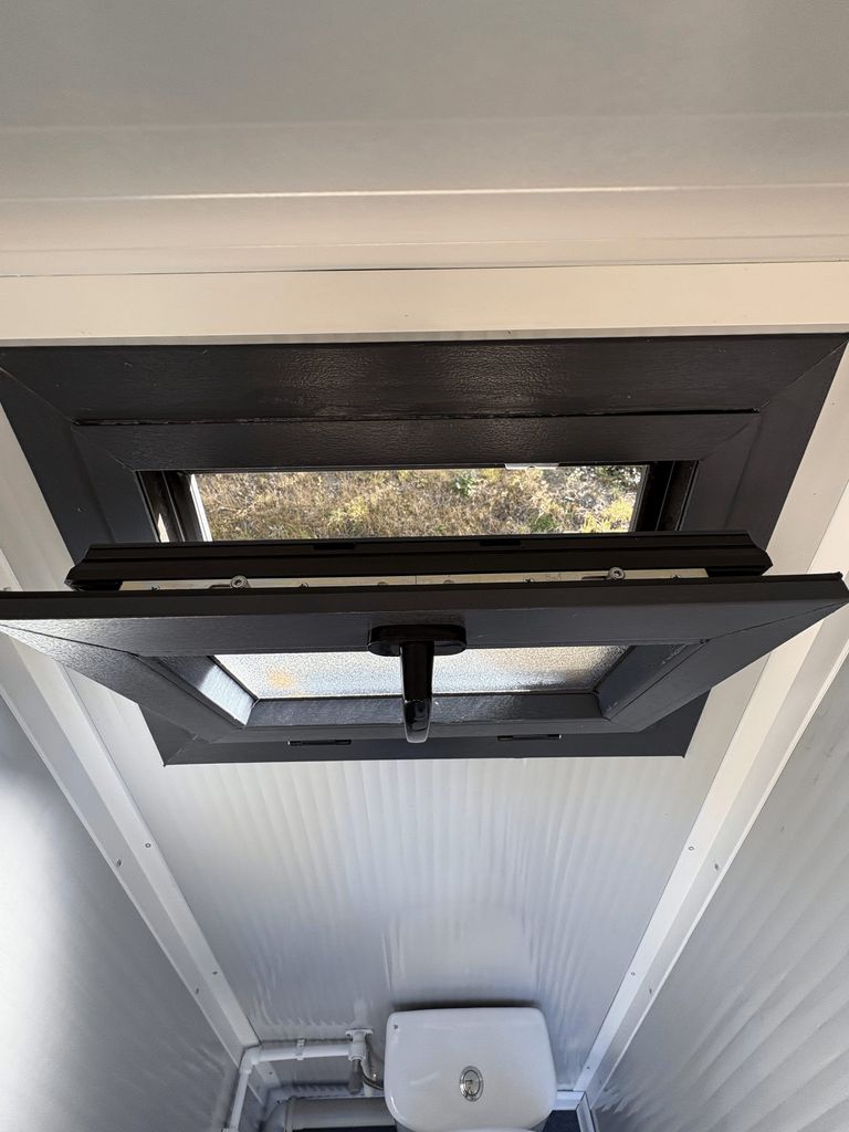 Exterior view of a portable toilet unit for camping with the window open.